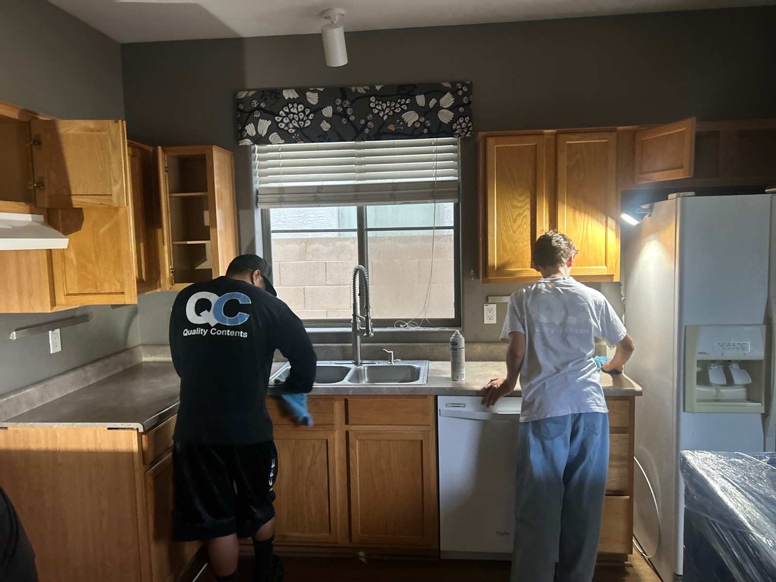 Two Quality Contents technicians in branded shirts cleaning a kitchen during a contents restoration job